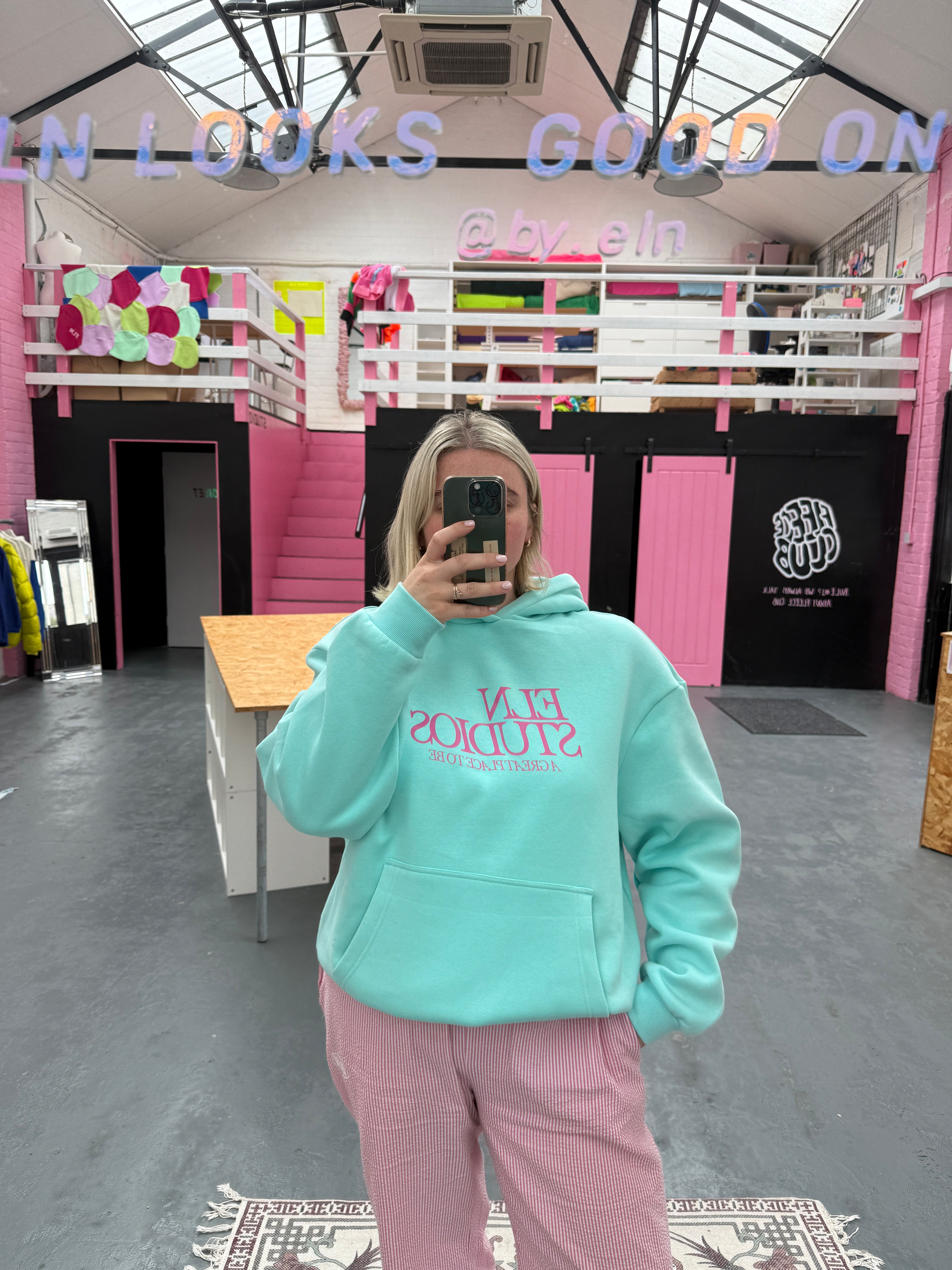 Person wearing a light blue hoodie with text, standing in a room with pink and black decor.